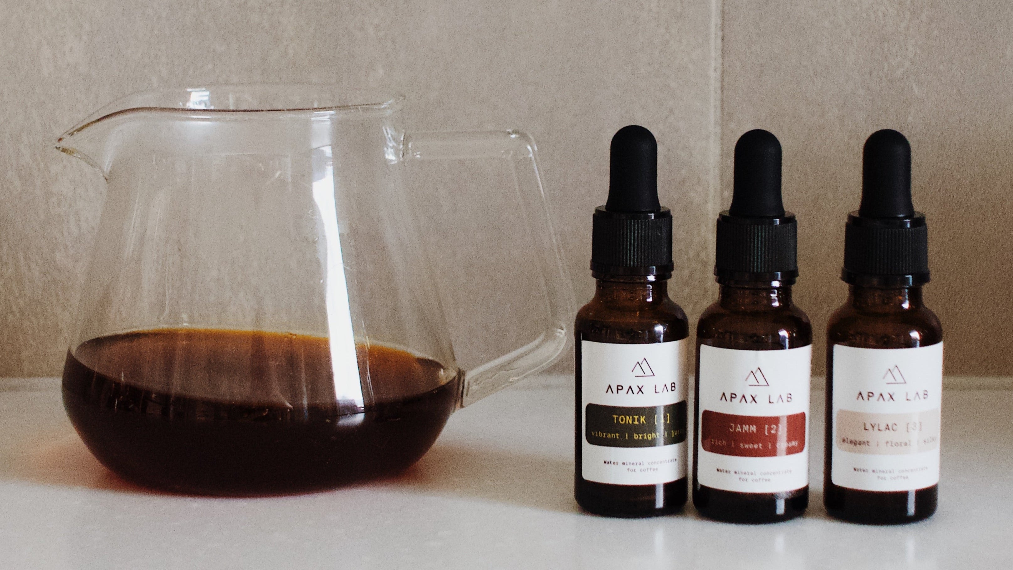 Apax Lab mineral blends placed next to a glass server of brewed specialty coffee, ready for use in water preparation